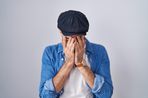 Free photo hispanic man with beard standing over isolated background with sad expression covering face with hands while crying depression concept