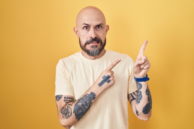 Free photo hispanic man with tattoos standing over yellow background pointing aside worried and nervous with both hands concerned and surprised expression