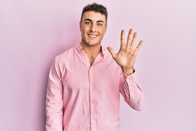 Hispanic young man wearing casual clothes showing and pointing up with fingers number five while smiling confident and happy