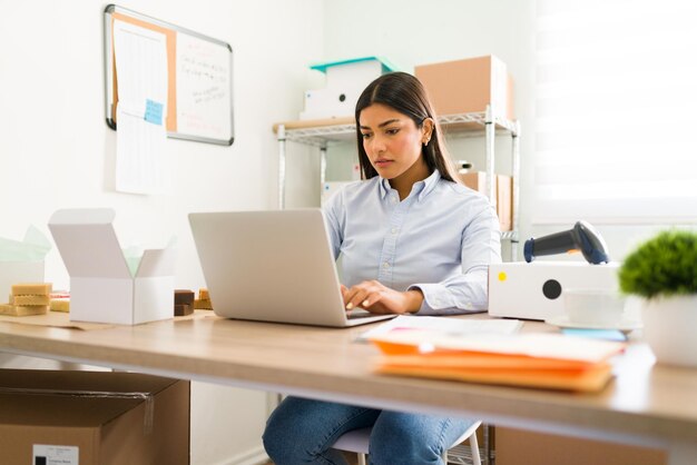 Hispanic young woman sitting at her office desk and working with her laptop. Young entrepreneur trying to succeed in the startup business