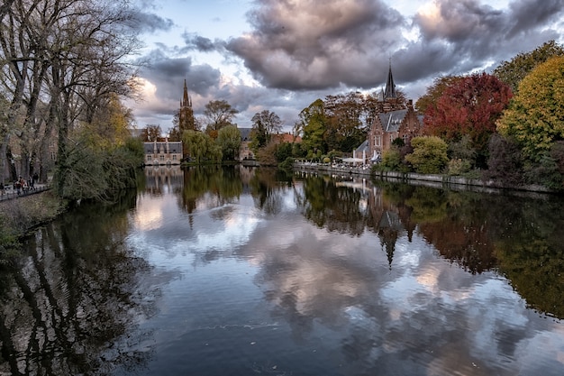 Free Photo historical castle surrounded by colorful trees reflected in the lake under the storm clouds