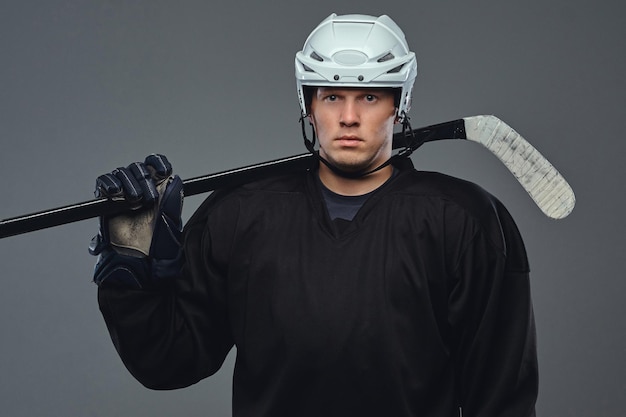 Free photo hockey player wearing black protective gear and white helmet holds a hockey stick. isolated on a gray background.