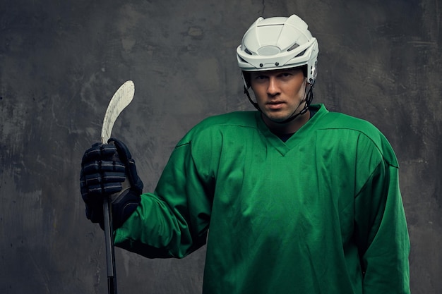 Free photo hockey player wearing green protective gear and white helmet standing with the hockey stick on a gray background.