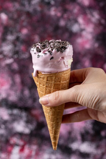 Holding a blueberry icecream in waffle cone on hand.