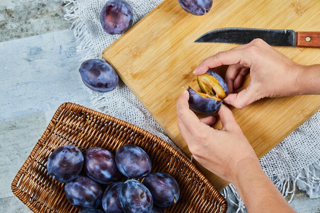 Holding fresh plum on wooden board with basket of plums