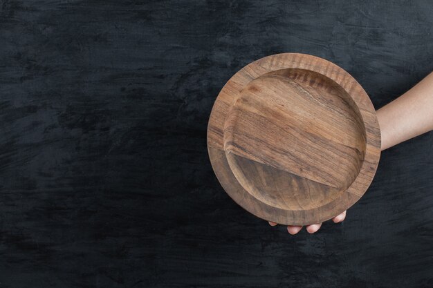 Holding a round wooden board on black background