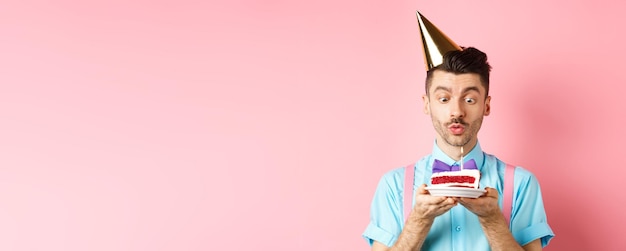 Free photo holidays and celebration concept happy young man in birthday party hat blowing candle on cake making