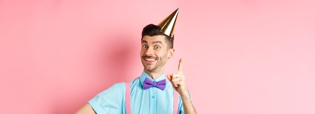 Free photo holidays and celebration concept image of happy man in birthday party hat pitching an idea raising f