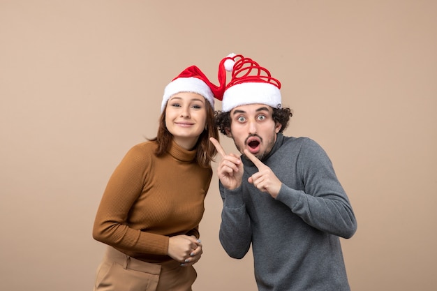 Free photo holidays festive and party concept - happy lovely shocked young couple wearing united each other santa claus hats on gray footage