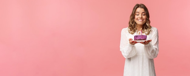 Free photo holidays spring and party concept portrait of dreamy happy birthday girl feeling excitement and joy celebrating bday biting lip and smiling as making wish blowing candle on cake