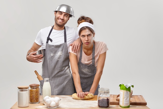 Free Photo home activities. tired housewife and husband prepare homemade cookies, knead dough for baking, follow recipe step at home, stand together at kitchen, isolated on white wall. culinary skills