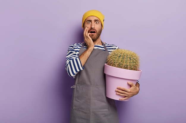 Free Photo home gardening concept. stupefied man holds big pot with cactus