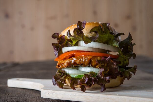 Home made chicken burger with lettuce, tomato and onion on wooden board.