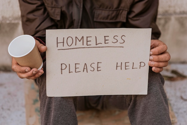 Free photo homeless man holding cup and help sign