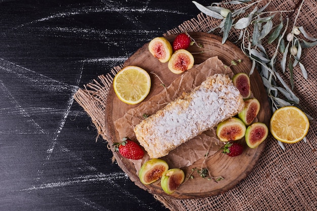 Homemade cake surrounded by various of fruits on round wooden platter. 