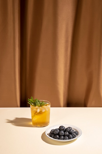 Homemade cocktail drink glass with blueberries on plate over white table near brown curtain