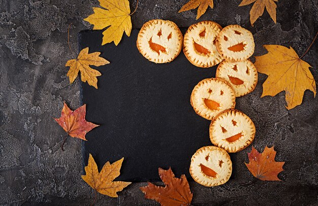 Homemade  cookies in the form as Halloween  jack-o-lantern pumpkins  on the dark table. Top view.