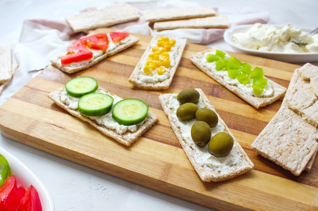 Free photo homemade crispbread toast with cottage cheese and green olives, slices of cabbage, tomatoes, corn, green pepper on cutting board. healthy food concept, top view. flat lay