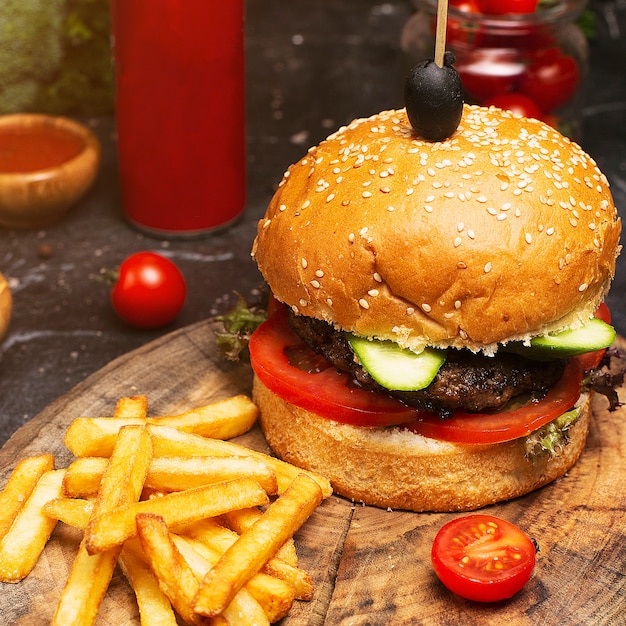 Homemade hamburger close-up with beef, tomato, lettuce, cheese and french fries on cutting board. Fastfood