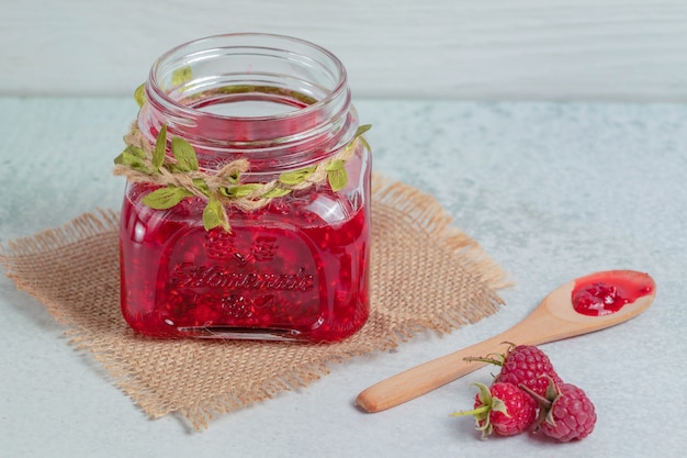 Homemade jam and fresh raspberry on grey surface.