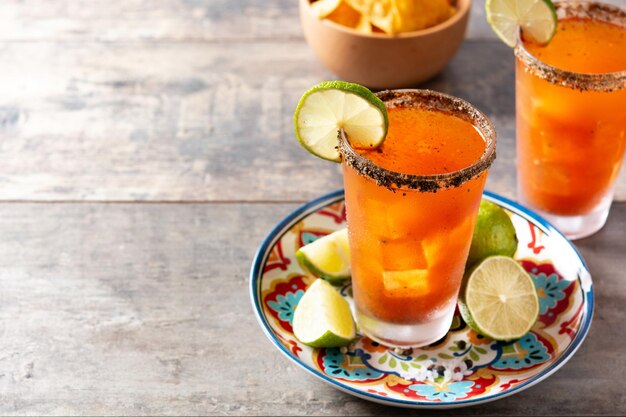 Homemade michelada cocktail with beer lime juicehot saucesalted rim and tomato juice on wooden table