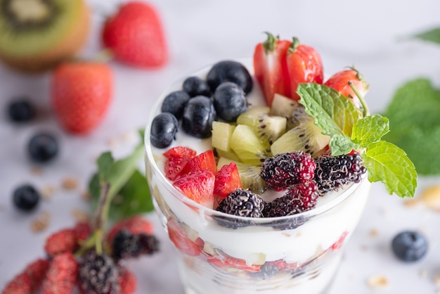 Homemade muesli, bowl of oat granola with yogurt, fresh blueberries, mulberry, strawberries, kiwi, mint and nuts board for healthy breakfast, copy space. Healthy breakfast concept. Clean eating.