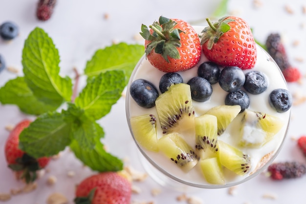 Free photo homemade muesli, bowl of oat granola with yogurt, fresh blueberries, mulberry, strawberries, kiwi, mint and nuts board for healthy breakfast, copy space. healthy breakfast concept. clean eating.