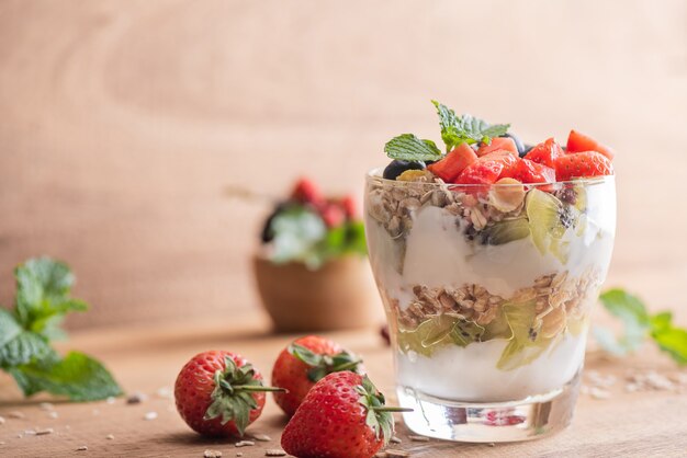 Homemade muesli, bowl of oat granola with yogurt, fresh blueberries, mulberry, strawberries, kiwi, mint and nuts board for healthy breakfast, copy space. Healthy breakfast concept. Clean eating.