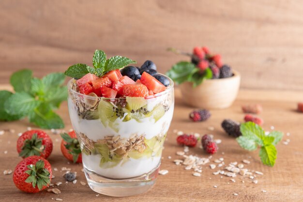 Homemade muesli, bowl of oat granola with yogurt, fresh blueberries, mulberry, strawberries, kiwi, mint and nuts board for healthy breakfast, copy space. Healthy breakfast concept. Clean eating.