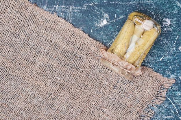 Free photo homemade pickled cucumbers in glass jar on blue with wool tablecloth.