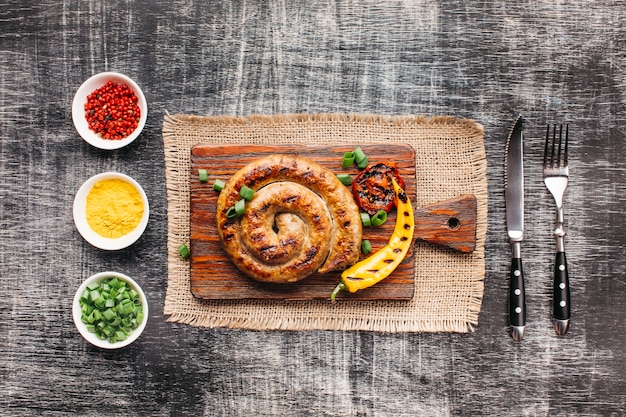 Homemade spiral grilled sausages on cutting board near healthy ingredient arranged in row