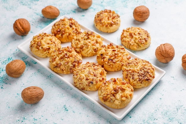 Homemade walnut cookies in white plate with walnuts on light table