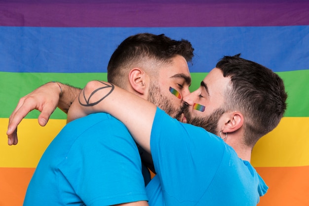 Homosexual couple of men hugging and kissing on rainbow flag