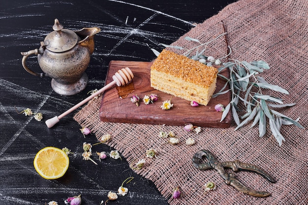 Honey cake on wooden board with dried flowers and teapot. 