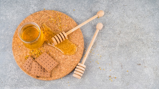 Honey pot; bee pollens; biscuits and honey dipper on coaster over the concrete backdrop