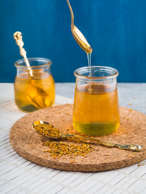 Honey pot with bee pollens on spoon over the cork coaster