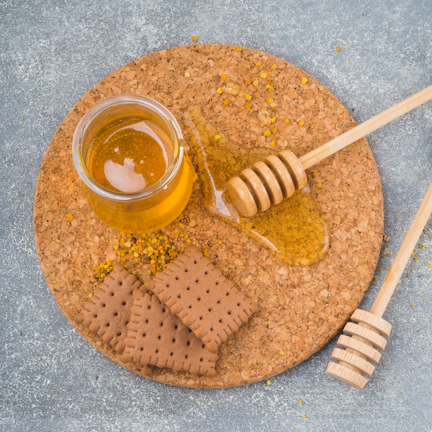 Free photo honey pot; wooden dipper; biscuits and bee pollen on cork coaster