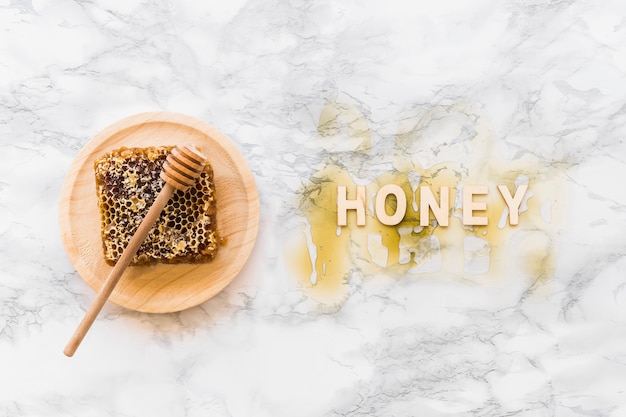 Free photo honey text with honeycomb and dipper on wooden plate over the white marble backdrop