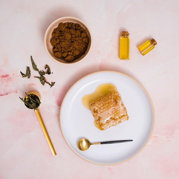 Honeycomb and honey on ceramic plate with cosmetics products against pink textured backdrop