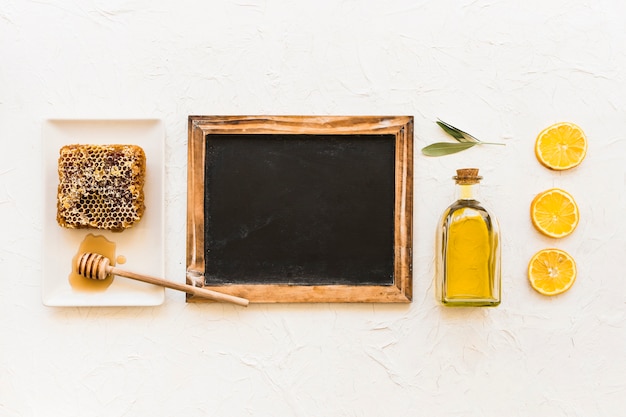 Free photo honeycomb, olive oil and lemon slices with dipper and empty slate