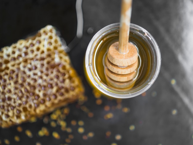 Free photo honeycomb piece and honey pot with wooden dipper on black backdrop