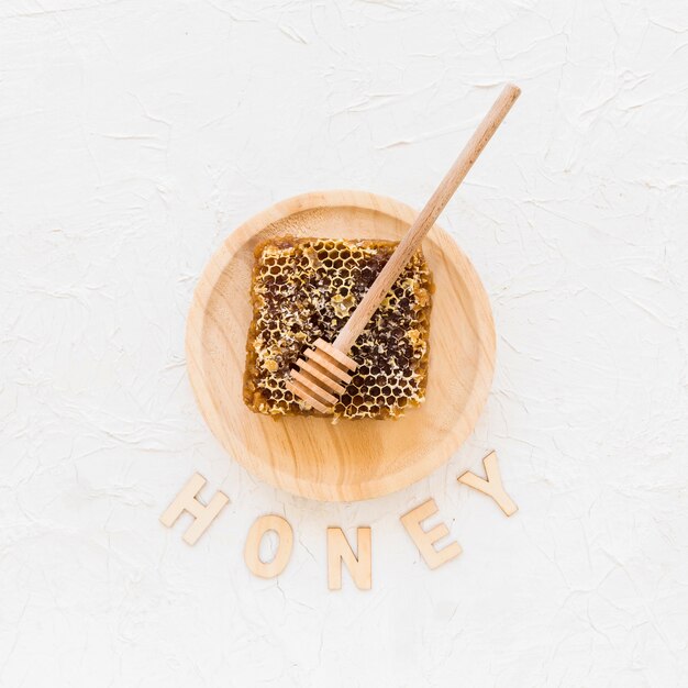 Honeycomb with wooden honey dipper on plate with text honey