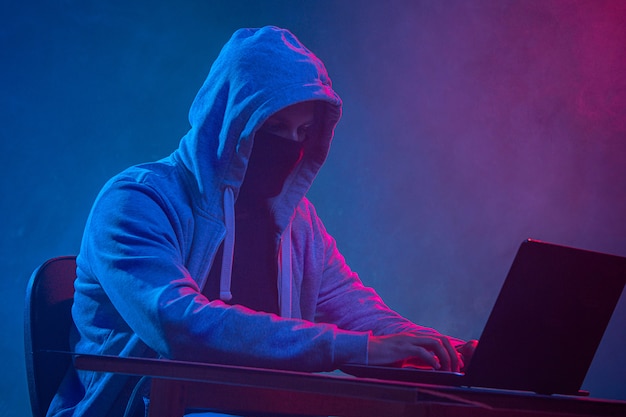 Free photo hooded computer hacker stealing information with laptop