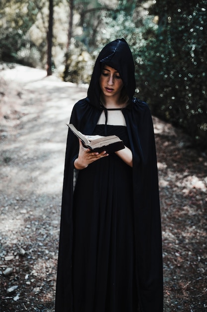 Hooded witch with book in forest daytime