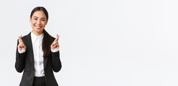 Hopeful businesswoman awaiting for promising results cross fingers good luck and smiling optimistic Happy saleswoman in black suit making wish anticipating good news white background