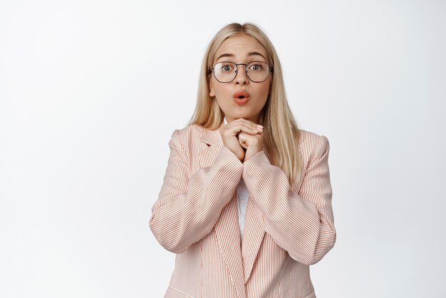 Hopeful businesswoman waiting with excitement looking fascinated awaiting relish standing in suit and glasses against white background