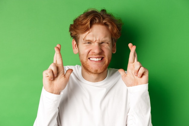 Free photo hopeful caucasian man looking worried, waiting for important results and making wish with fingers crossed, standing over green background