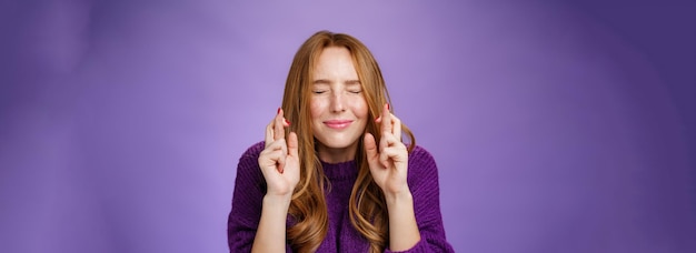 Hopeful and dreamy cute tender redhead s girl in purple sweater making wish faithfully close eyes an