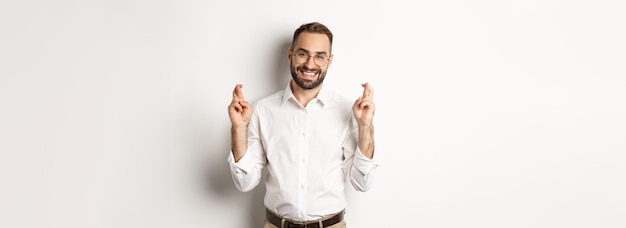 Free photo hopeful optimistic man making a wish cross fingers and praying standing over white background