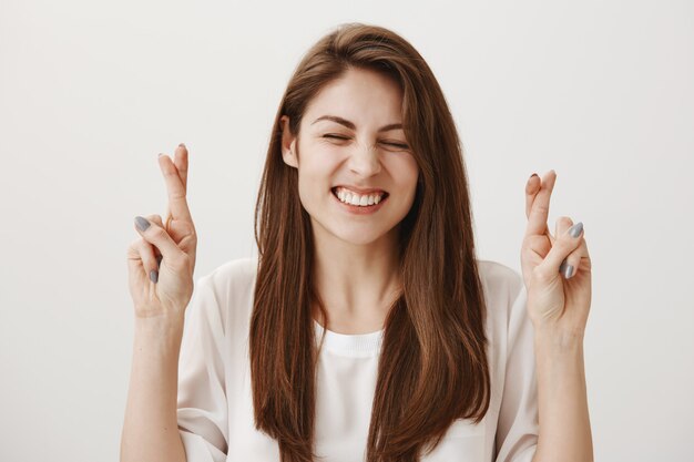 Hopeful positive girl cross fingers while making wish, smiling optimistic